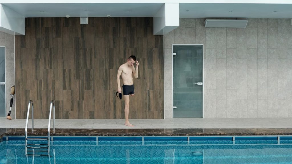 Amputee athlete preparing at an indoor swimming pool, portraying determination and fitness.